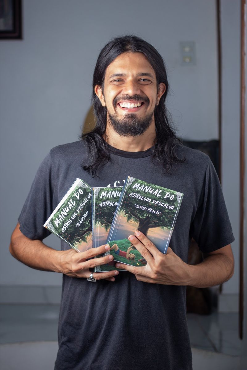 Daniel Paiva, astrólogo, segurando os três volumes do livro Manual do Astrólogo Descalço